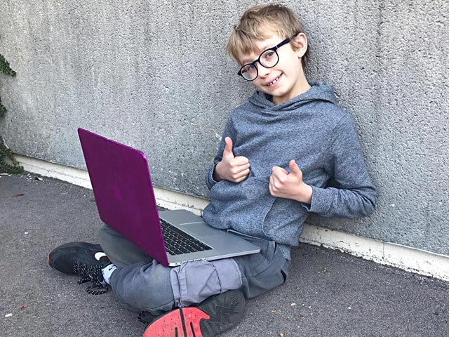 a student editing on a laptop outside and giving a thumbs up
